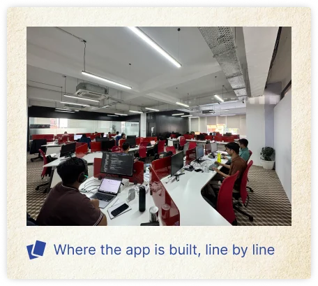 A modern software development office with programmers working at rows of red and white desks equipped with computer monitors and laptops. The image includes the caption “Where the app is built, line by line,” highlighting a collaborative environment where an app is developed and coded.